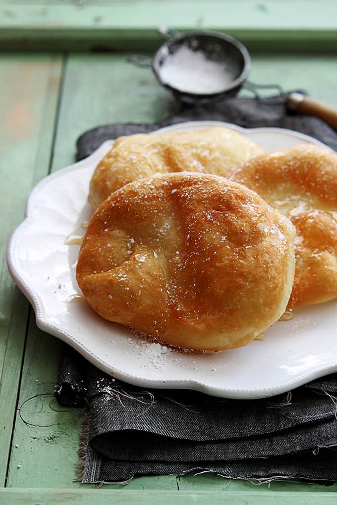 fried scones on a plate topped with honey and powdered sugar.