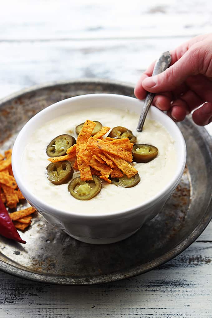 jalapeño popper chicken soup in a bowl with a hand holding a spoon in the soup.