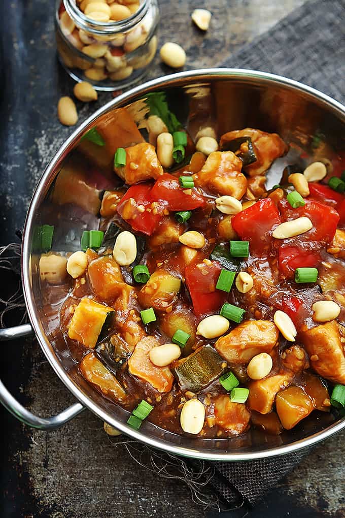 top view of slow cooker kung pao chicken in a metal bowl topped with peanuts with more peanuts on the side in a small jar.