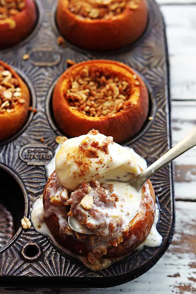 peach crisp stuffed baked peaches in a muffin tin with the front peach topped with ice cream and a spoon.