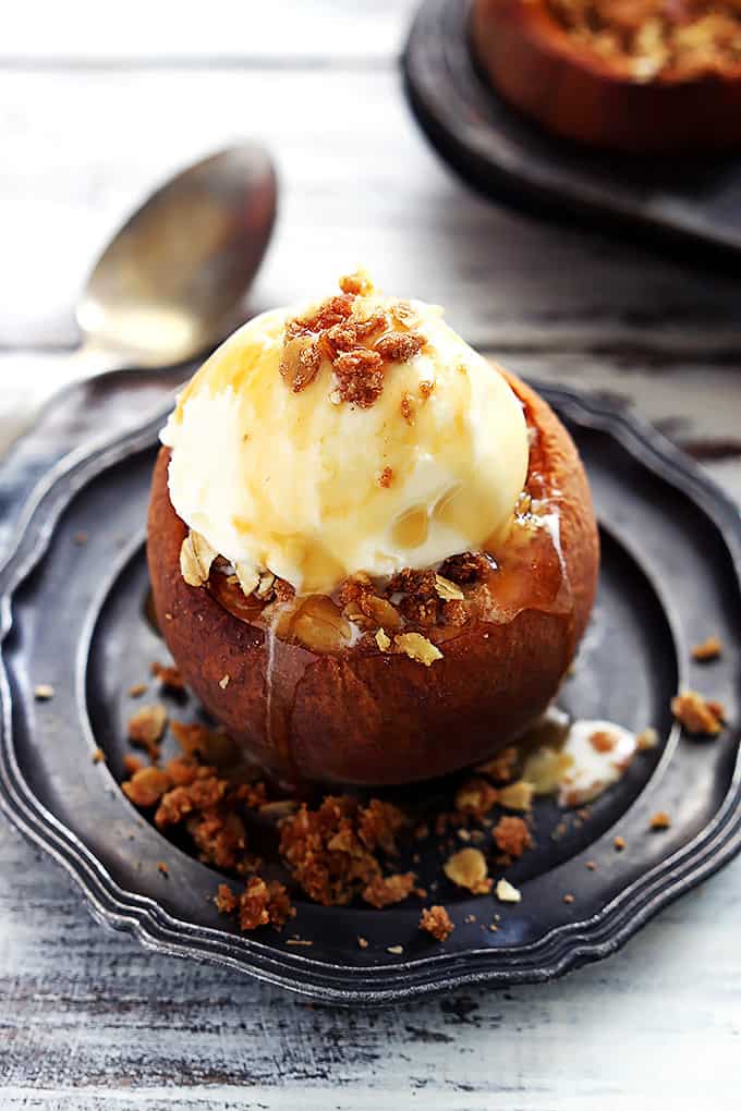 a peach crisp stuffed baked peach topped with ice cream on a plate with a spoon on the side.