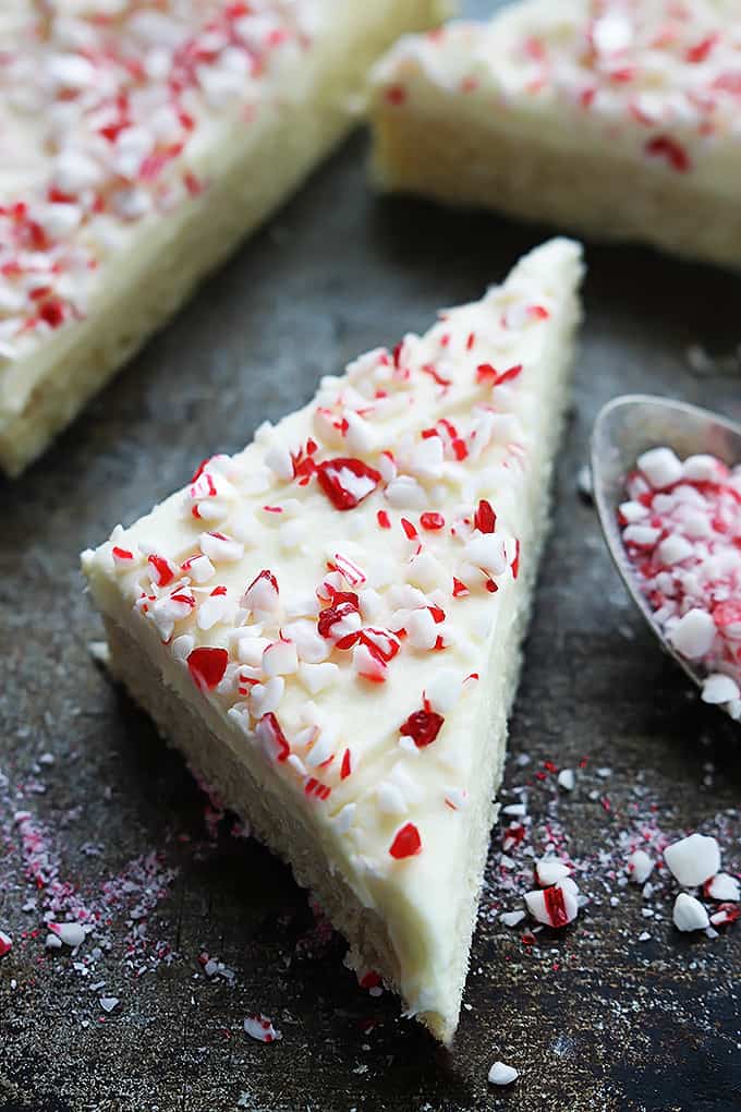 a peppermint crunch sugar cookie bar on the side of a spoon filled with peppermint chunks and more bars in the background.