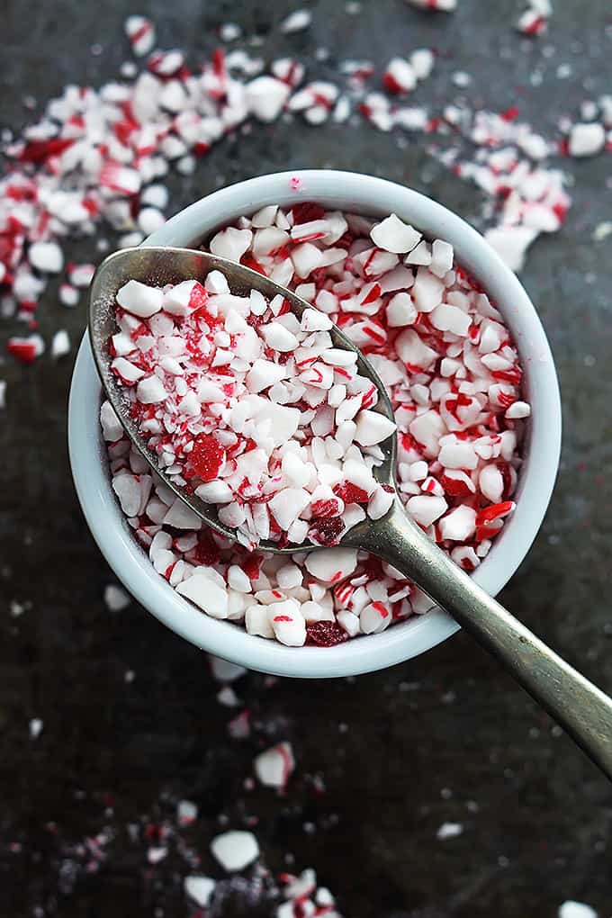 top view of a bowl of peppermint chunks with a spoon sitting on top more peppermint chunks on top.