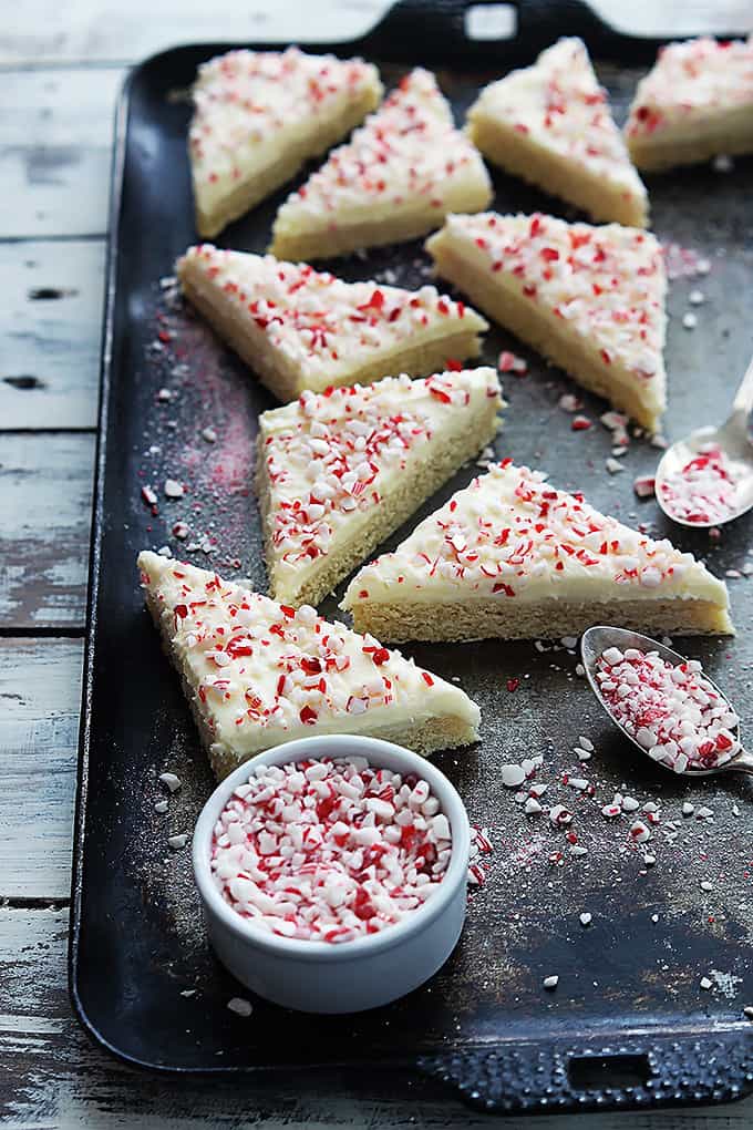 peppermint crunch sugar cookie bars on a baking sheet with a bowl and spoons filled with peppermint chunks.