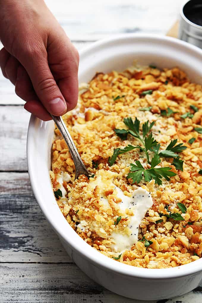 a hand scooping out some poppy seed chicken casserole with a spoon from a serving dish.