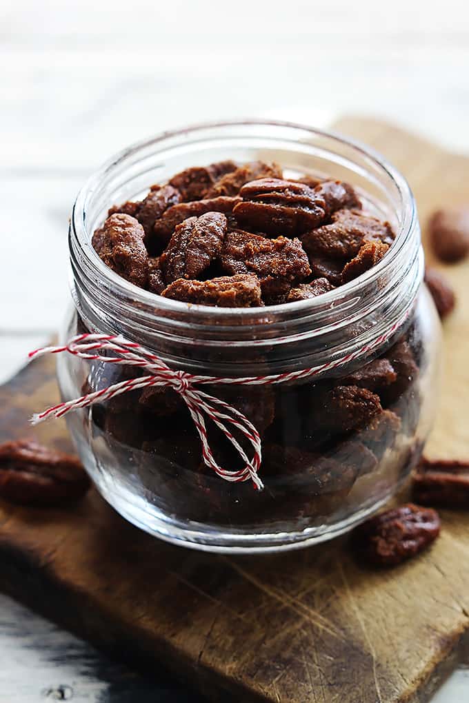 slow cooker cinnamon pecans in a small mason jar on a wooden cutting board.