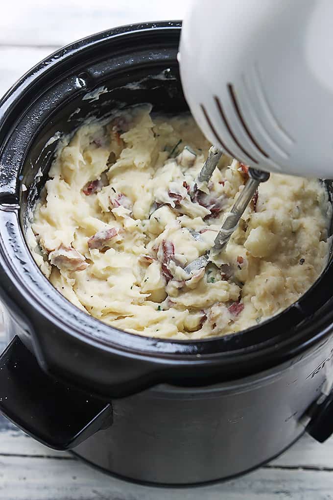 top view of a blender being held above ingredients just mixed together in a slow cooker.