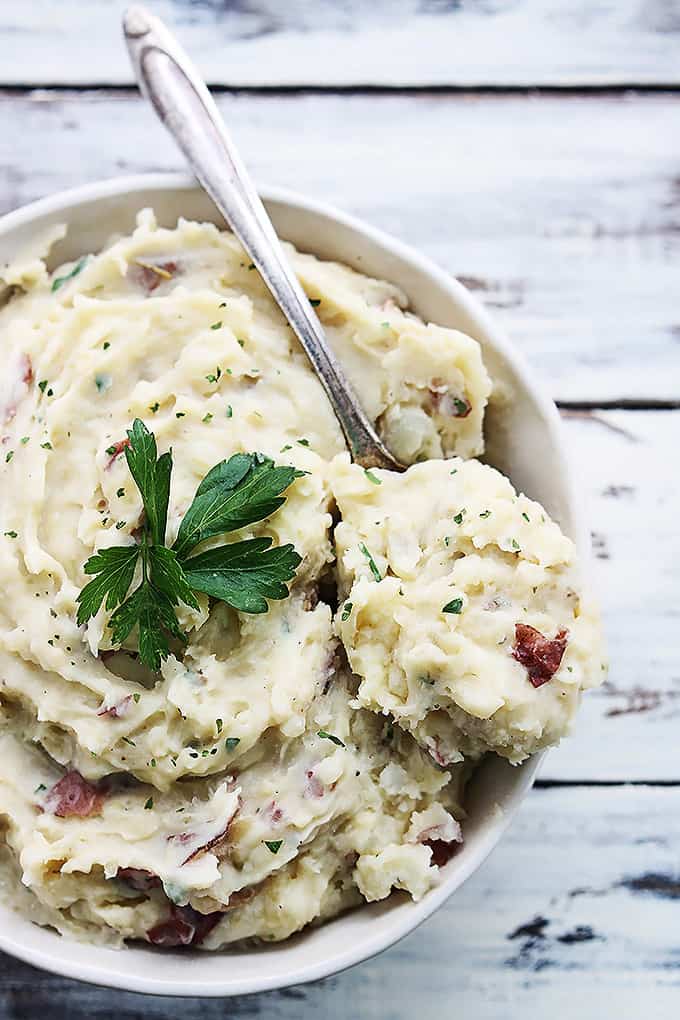 top view of slow cooker buttery garlic herb mashed potatoes with a spoon in a bowl.