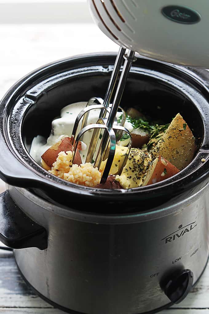 a blender being held above raw ingredients in a slow cooker.