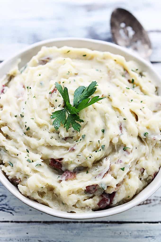 top view of slow cooker buttery garlic herb mashed potatoes in a bowl with a spoon on the side.