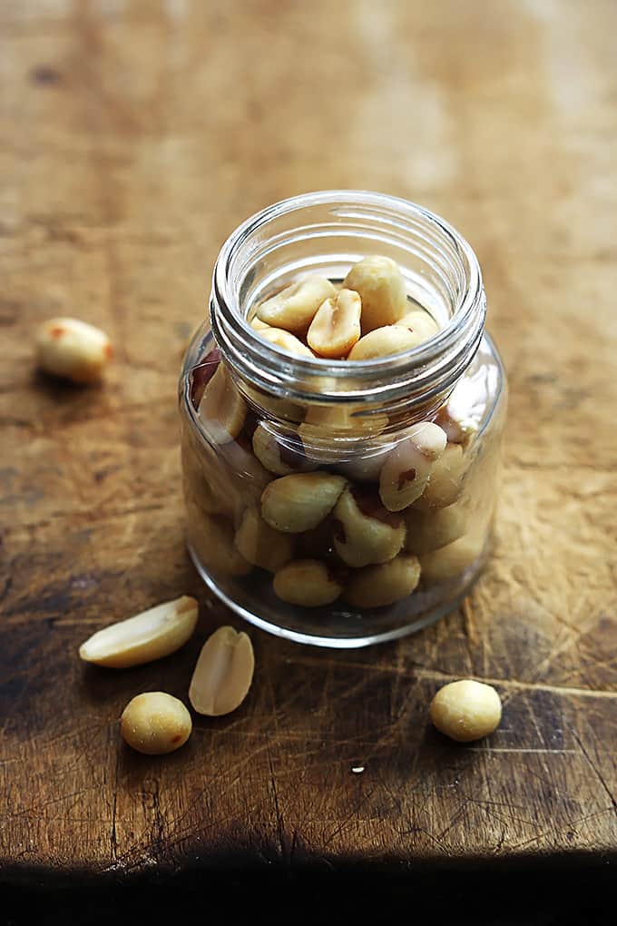 a small jar full of peanuts with more peanuts on the side.