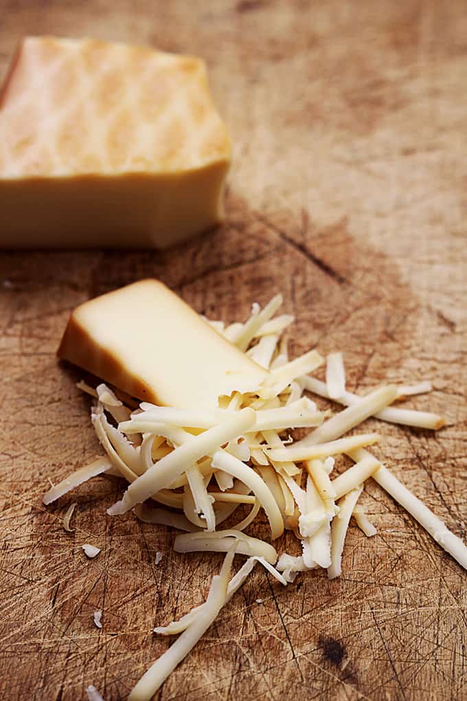 a block of cheese that's half shredded on a cutting board.