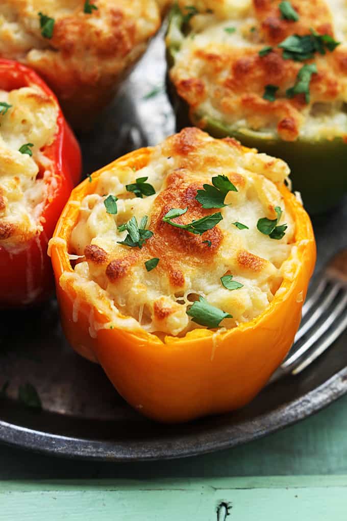 close up of three cheese macaroni stuffed peppers and a fork on a round serving tray. 