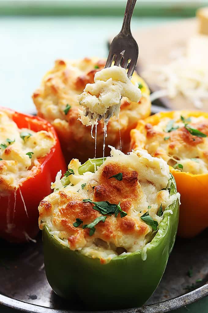 three cheese macaroni stuffed peppers with a fork with a bite of macaroni on it above the front pepper.