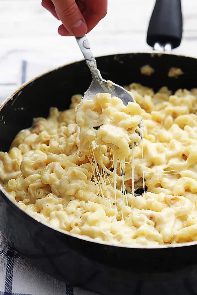 a hand scooping a spoonful of three cheese macaroni from a skillet.