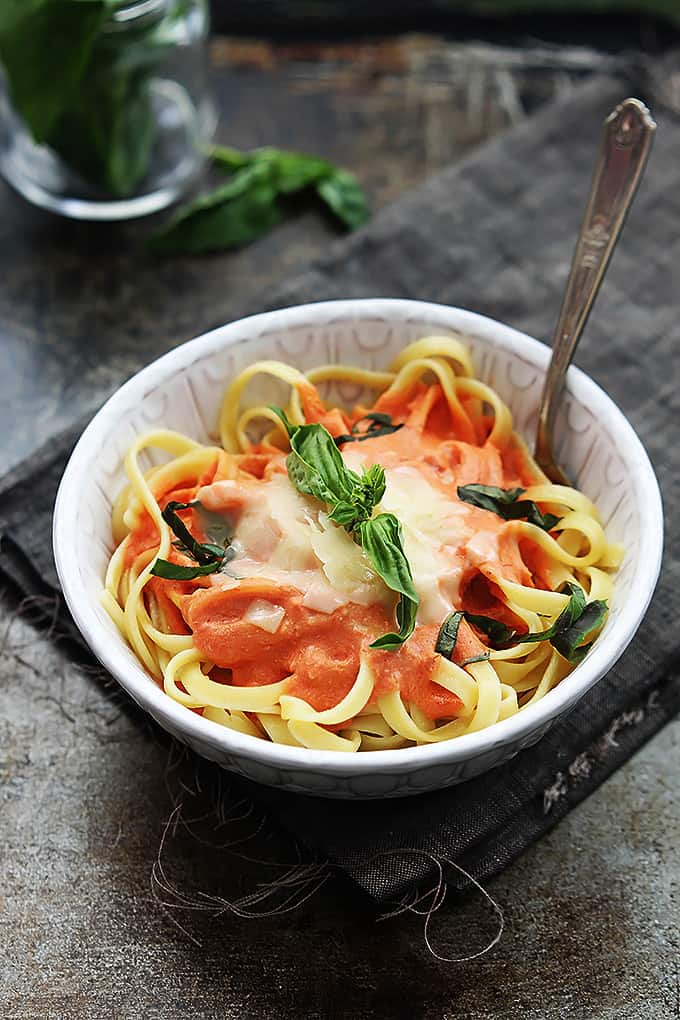 creamy tomato basil fettuccini with a fork in a bowl on a cloth napkin.