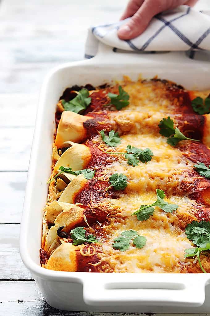 turkey enchiladas in a baking dish with a hand holding one of the handles on the side with a hot pad.