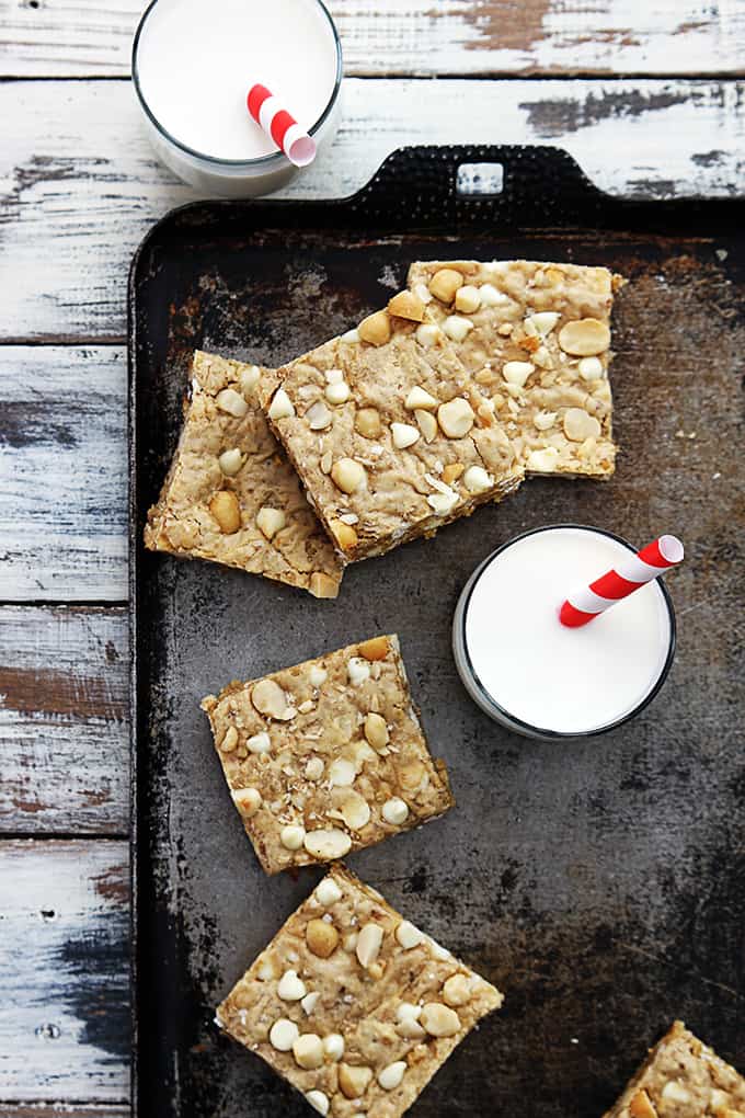 top view of white chocolate chip macadamia nut blondies on a baking sheet with a glass of milk with a straw and another glass of milk on the side of the  baking sheet.