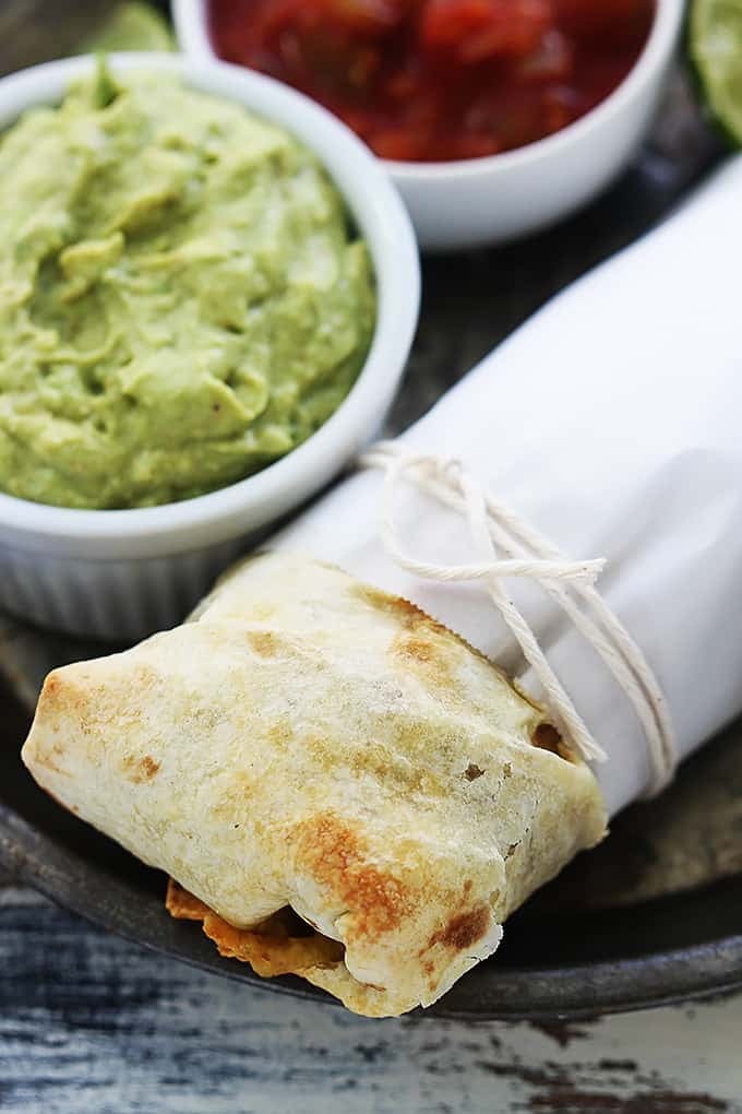 a baked chicken chimichanga with a bowl of guacamole on the side.