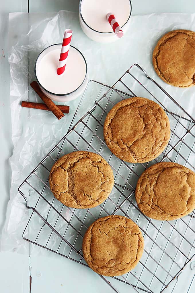 top view of caramel stuffed snickerdoodles on a cooling rack with a couple glasses of milk and cinnamon sticks on the side.