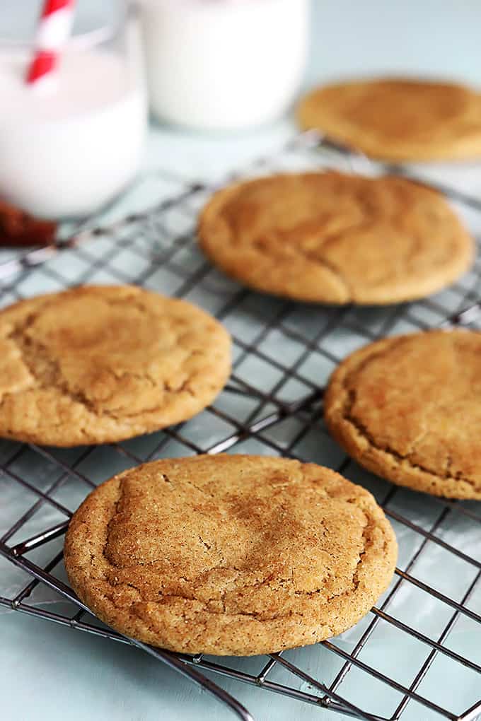 caramel stuffed snickerdoodles on a cooling rack with a couple glasses of milk on the side.