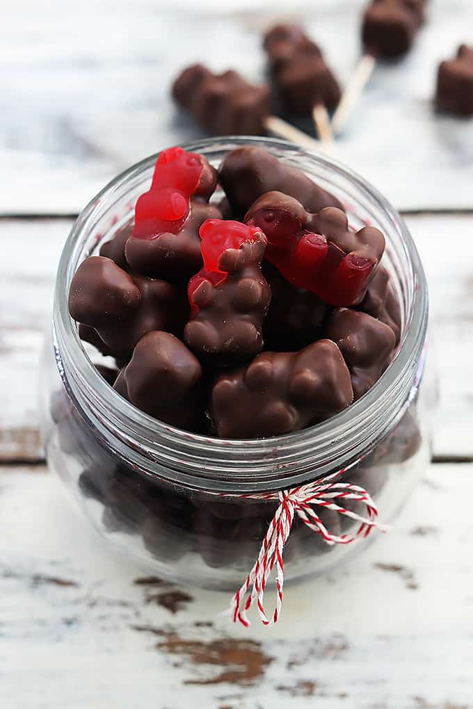 chocolate covered cinnamon bears in a jar with more bears on toothpicks in the background.