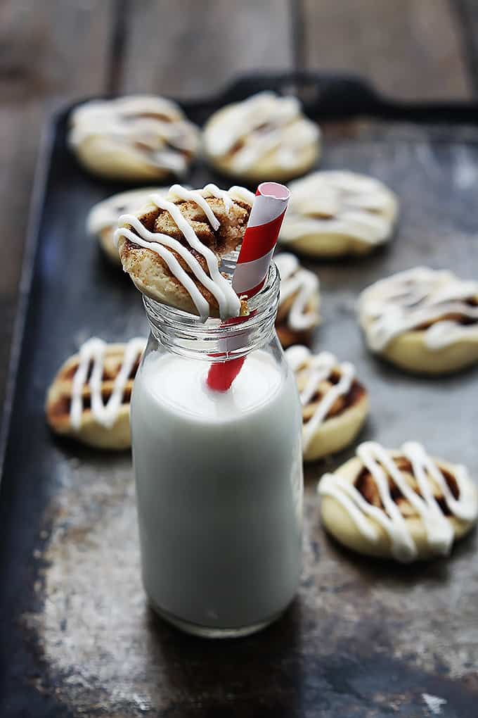 a glass jar with a cinnamon roll cookie sitting on top with a bite taken out of it with more cookies on the side.