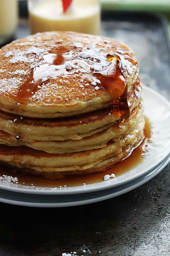 a stack of eggnog pancakes on a plate topped with powdered sugar and syrup.