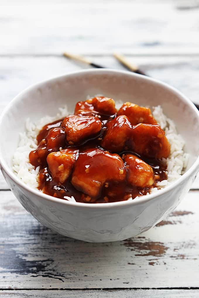 honey sriracha chicken on rice in a bowl with chopsticks in the background.