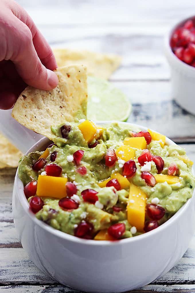 a hand dipping a chip in a bowl of mango pomegranate guacamole.