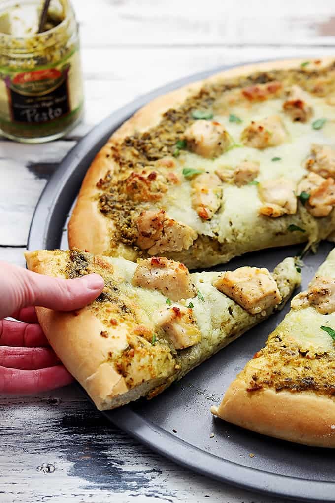 a hand taking a slice of pesto chicken pizza.