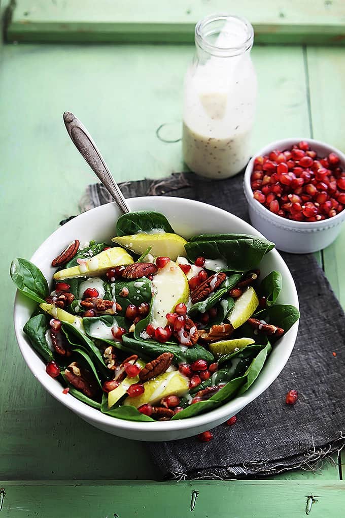 pomegranate pear & pecan salad with poppyseed dressing with a fork in a bowl with a bowl of pomegranate and poppyseed dressing in the background.