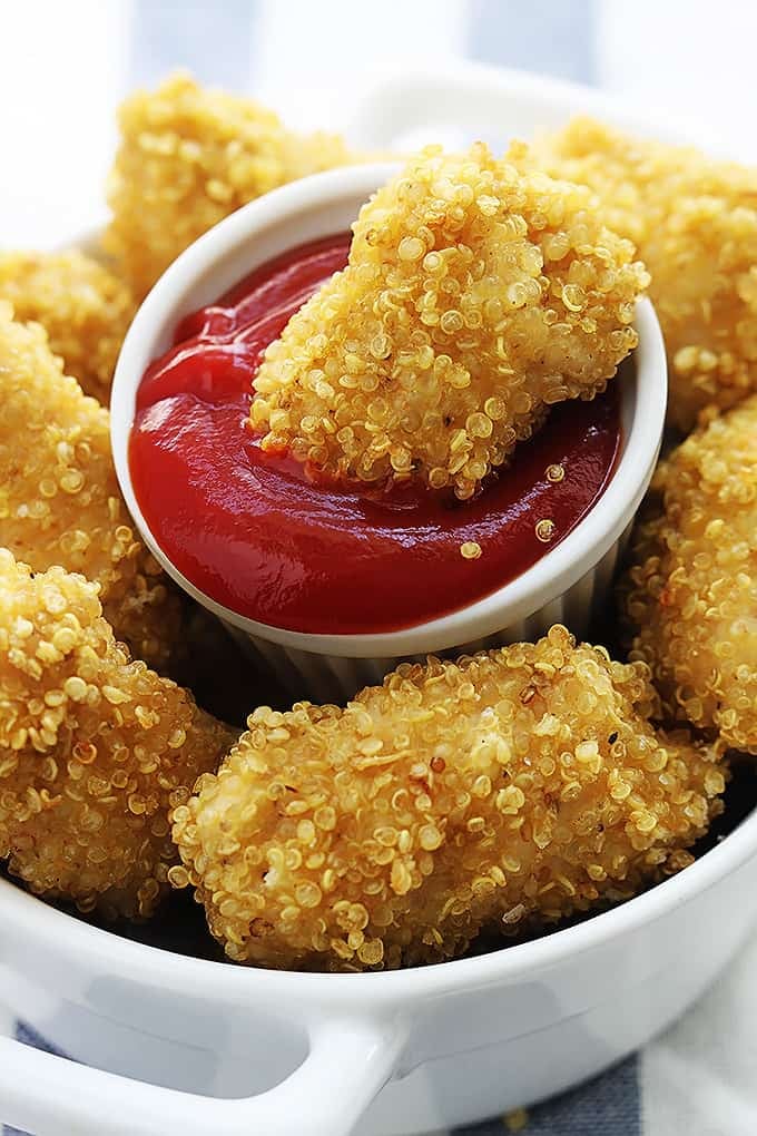 quinoa chicken nuggets in a bowl with a small dipping bowl of ketchup in the middle with a chicken nugget dipped in it.