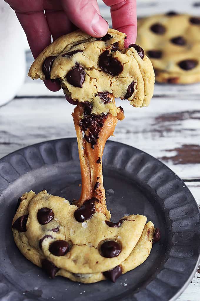 a hand pulling half of a salted caramel chocolate chip cookie from the other half on a plate.