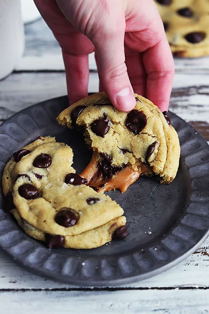 a salted caramel chocolate chip cookie split in half on a plate with a hand grabbing one of the halves.