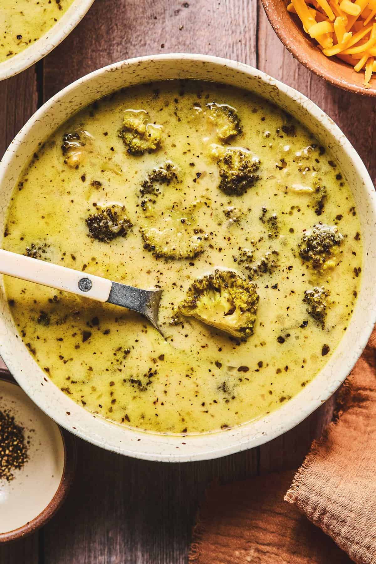 Overhead of slow cooker broccoli cheddar cheese soup and a spoon in a bowl.