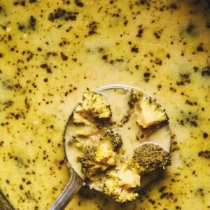 Close up overhead of a label lifting up some slow cooker broccoli cheddar cheese soup from a slow cooker full of soup.