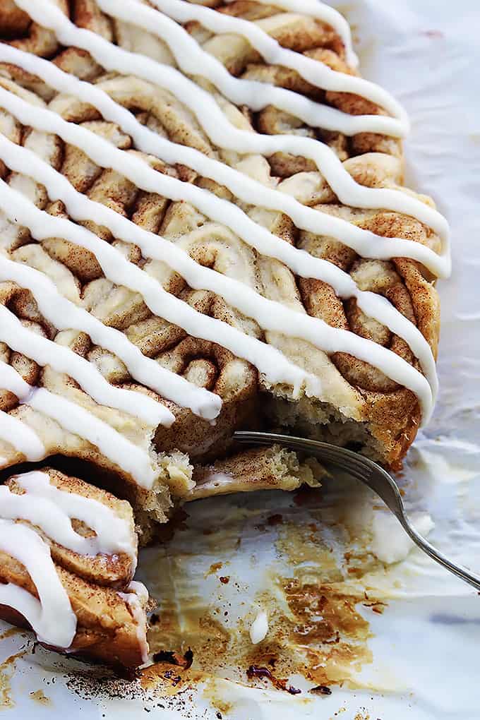 close up of slow cooker cinnamon rolls topped with icing with some rolls missing and a fork on the side.