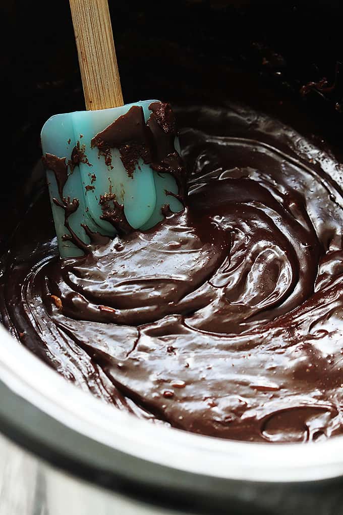 close up of cooked slow cooker fudge ingredients in a slow cooker with a spatula.