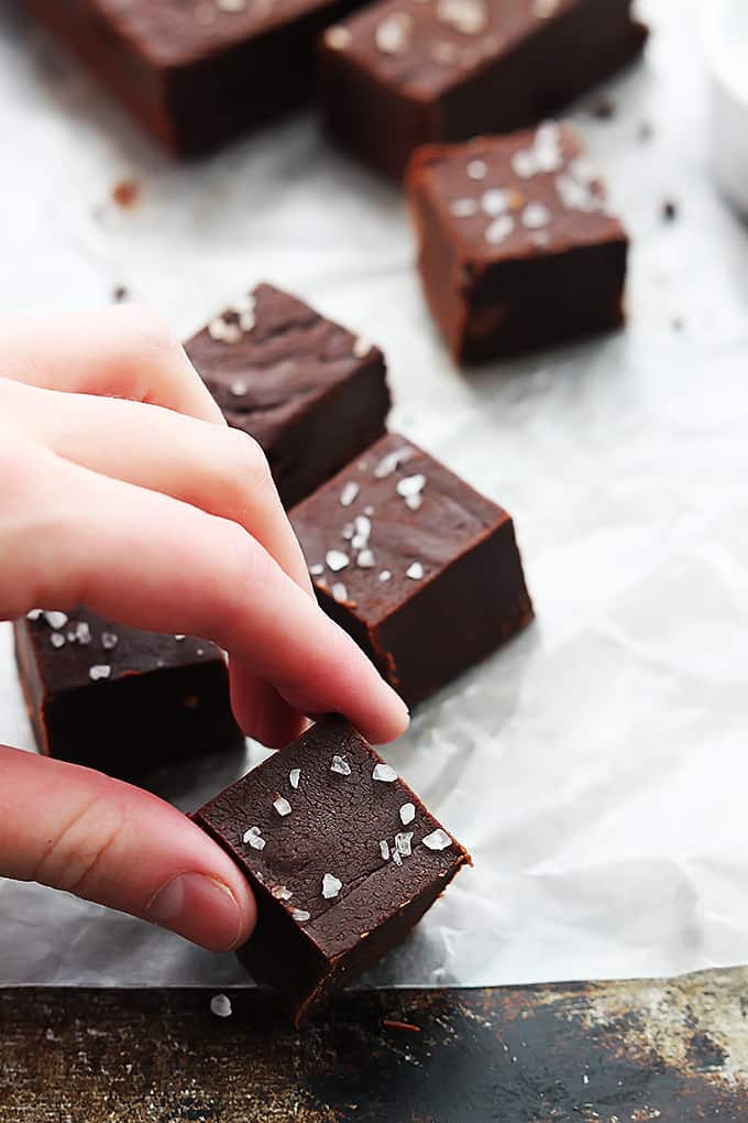 a hand picking up a slow cooker fudge cube with more fudge in the background.