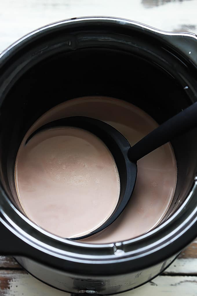 top view of slow cooker salted caramel hot chocolate in a slow cooker with a serving spoon.