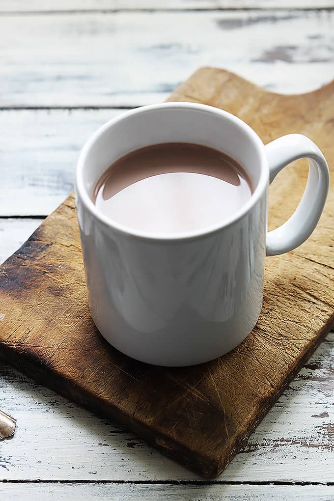 slow cooker salted caramel hot chocolate in a mug on a wooden cutting board.