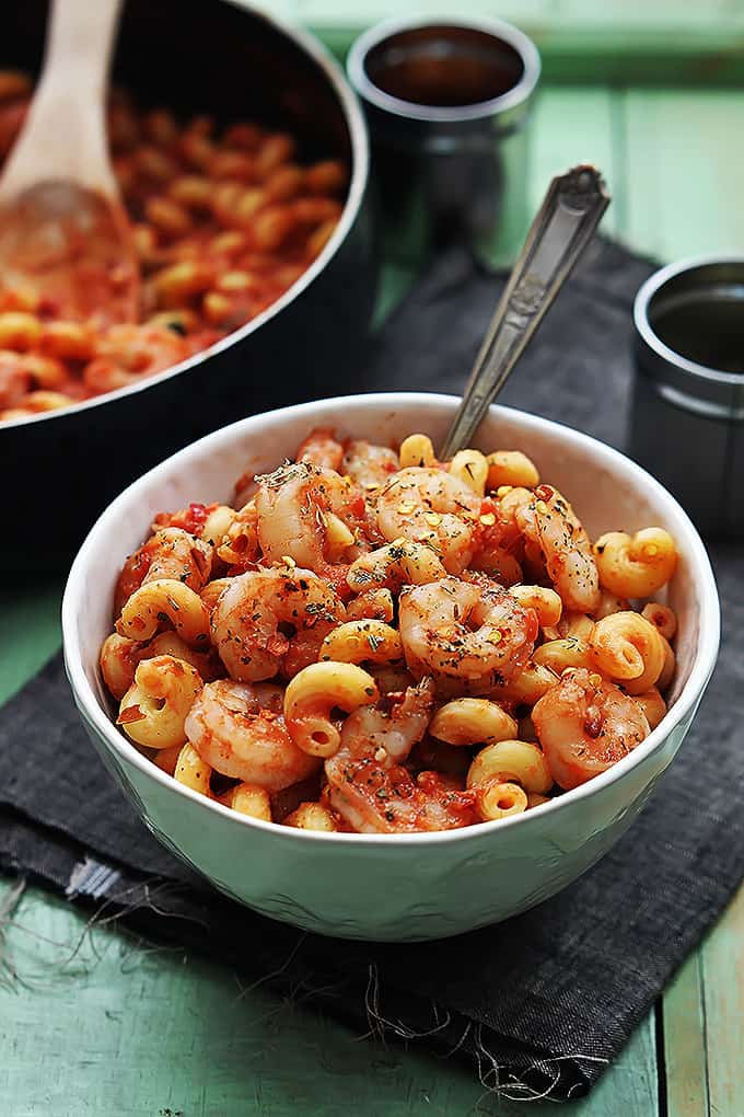 a bowl of spicy tomato garlic shrimp pasta with a skillet with more pasta in the background.