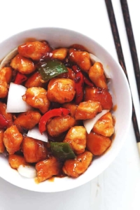 sweet and sour chicken with onions and bell peppers in a white bowl with chopsticks