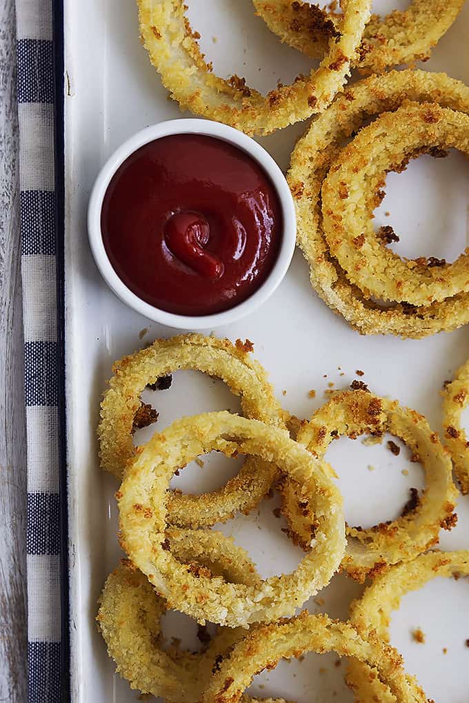 top view of onion rings on a baking sheet with a small dipping sauce bowl of ketchup on the side.