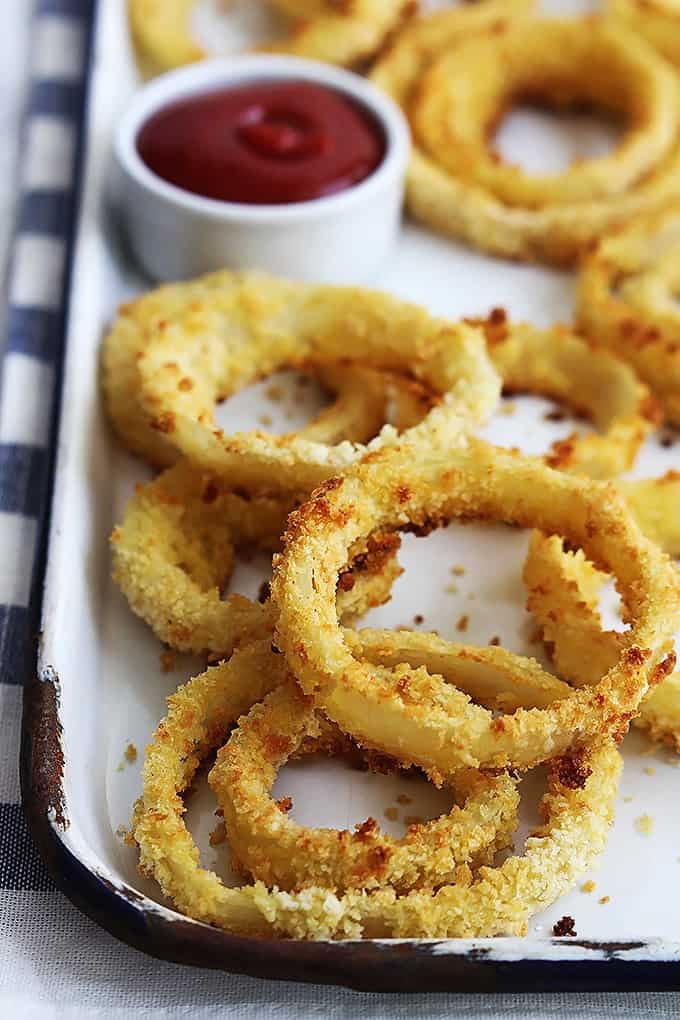 close up of onion rings on a baking sheet with a dipping bowl of ketchup on the side.