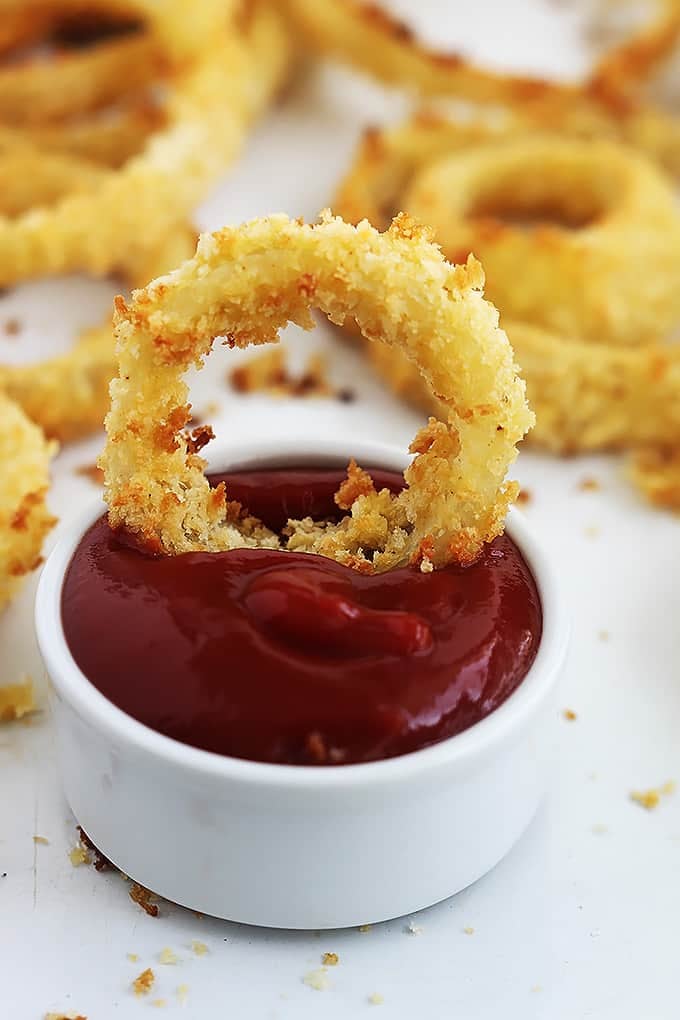 an onion ring sitting in a bowl of ketchup with more onion rings in the background.