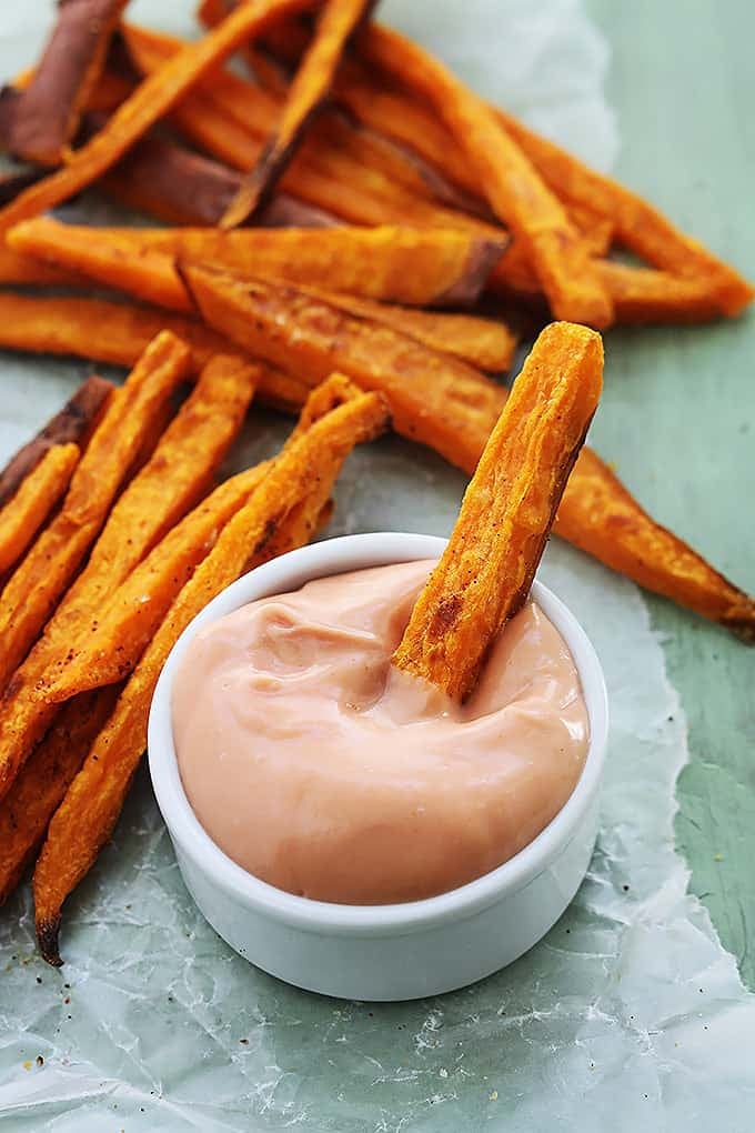 a sweet potato fry dipped in bowl of fry sauce with more fries in the background.