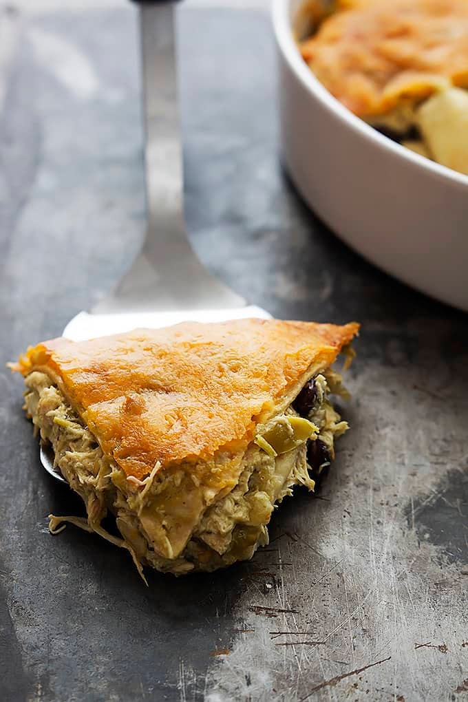 a spatula with a slice of chicken verde tortilla pie on top with the rest of the pie in a round serving pan on the side.