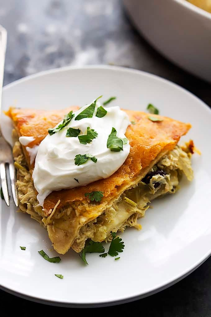 chicken verde tortilla pie topped with sour cream with a fork on a plate.